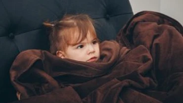 Little girl wrapped in a brown blanket.