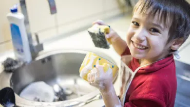 Little boy smiling while washing the dishes