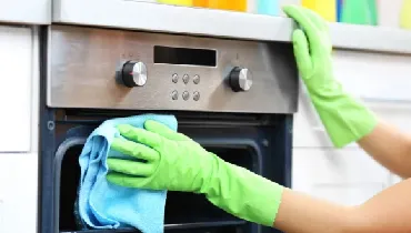 Person wearing protective gloves and cleaning an oven.