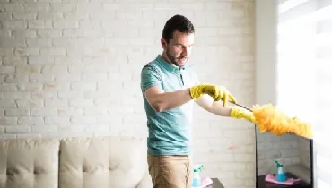 Man dusting his living room furniture.