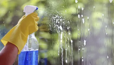 Person spraying cleaning solution on a window