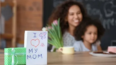 Greeting card and gift for Mother's Day on table in kitchen