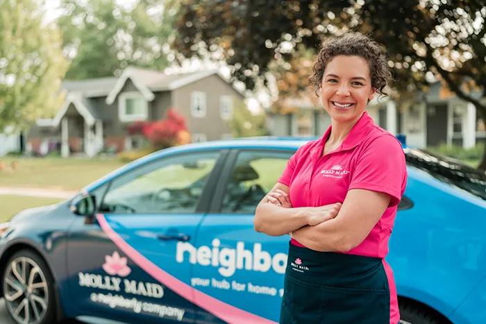 A Molly Maid professional standing by a company car and smiling before a cleaning service appointment.