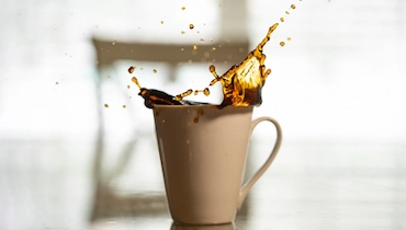 Coffee splashing out of tan mug.