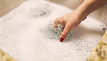 Close-up of manicured hand with red nail polish soaking crystal glass in tub of water.