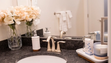 Black granite top bathroom sink with white hand soap dispenser and vase of flowers.