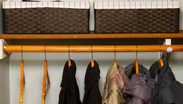 Close-up of two black wool coats and three puffer coats on wooden hangers in organized hall closet.