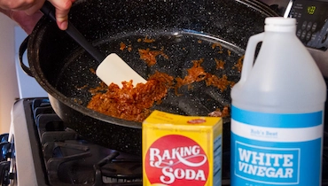 Close-up of roasted food being scraped off bottom of pan with rubber spatula.