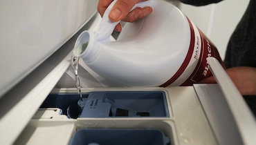 Person pouring chlorine bleach into automatic dispenser in washer.