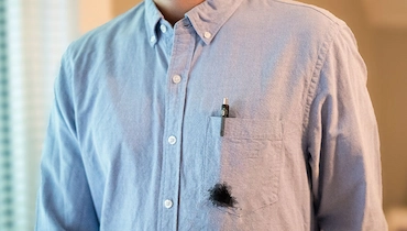 Close-up of man in blue button down shirt with pen in breast pocket leaking spot of black ink.