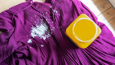 Overhead view of purple dress with large white stain and yellow container of stain remover.