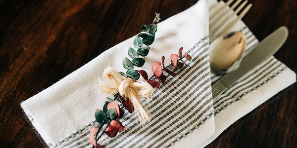 Set of cutlery folded into linen napkin with pair of dried decorative branches rested atop.