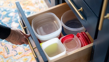 Elderly person's hand opening drawer full of organized Tupperware.