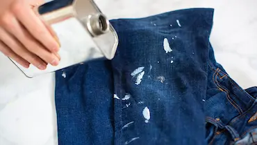 Close-up of person holding steel canister over blue jeans stained with white paint.