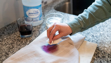 Close-up of person's hand blotting grape juice stain out of fabric with ammonia.