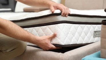 Closeup of person lifting a corner of the mattress off of a bed frame.