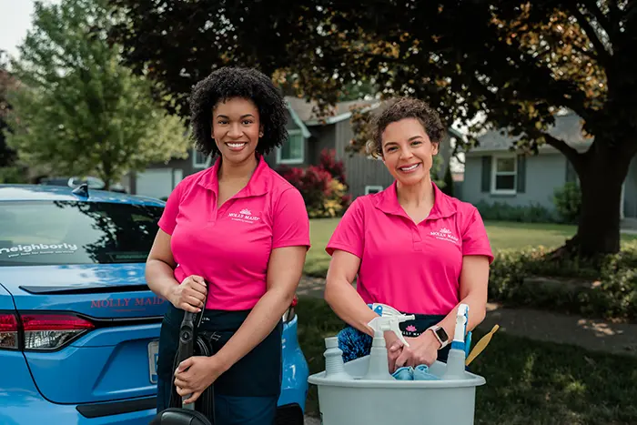 Molly Maid professionals outside holding supplies and smiling before providing cleaning service. 