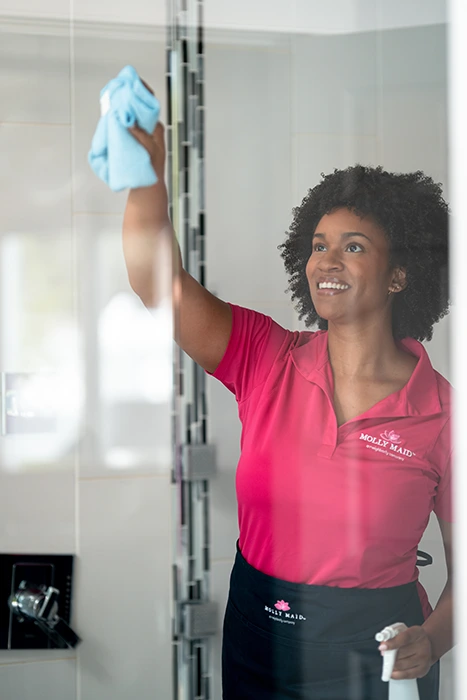 A Molly Maid professional wiping a shower door at a move-out cleaning appointment.