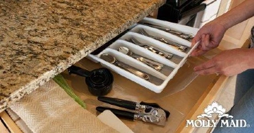 A person organizing a kitchen drawer containing silverware in a tray and utensils.